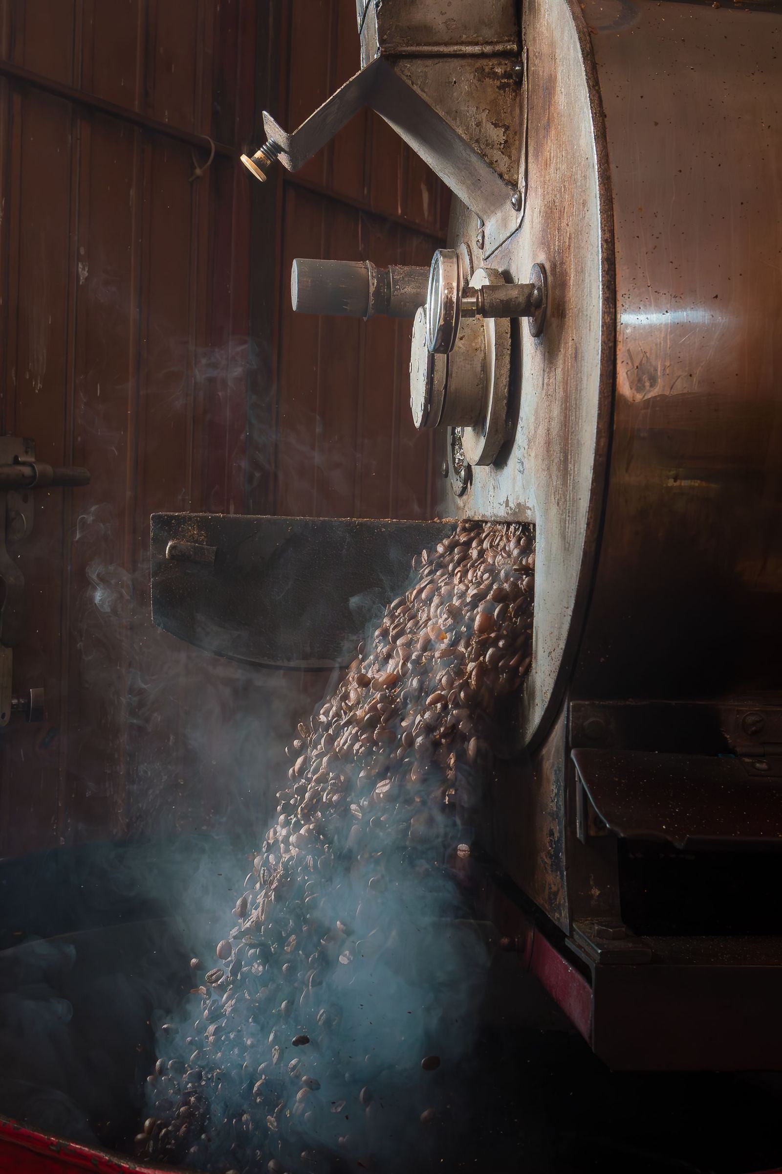 Beans tumbling out of a roaster in a cloud of steam.