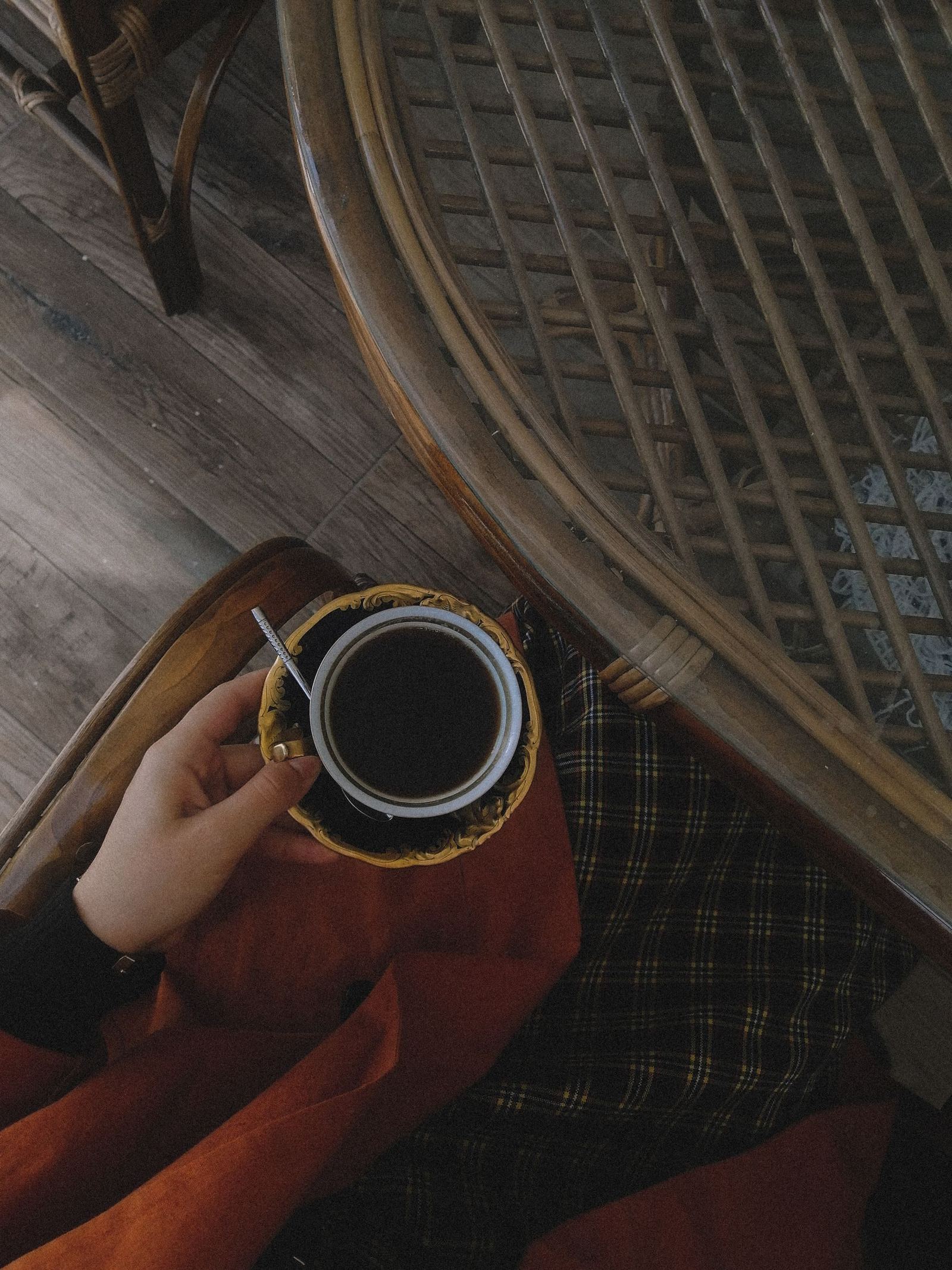 Hands wrapped around a black cup on a woven surface.