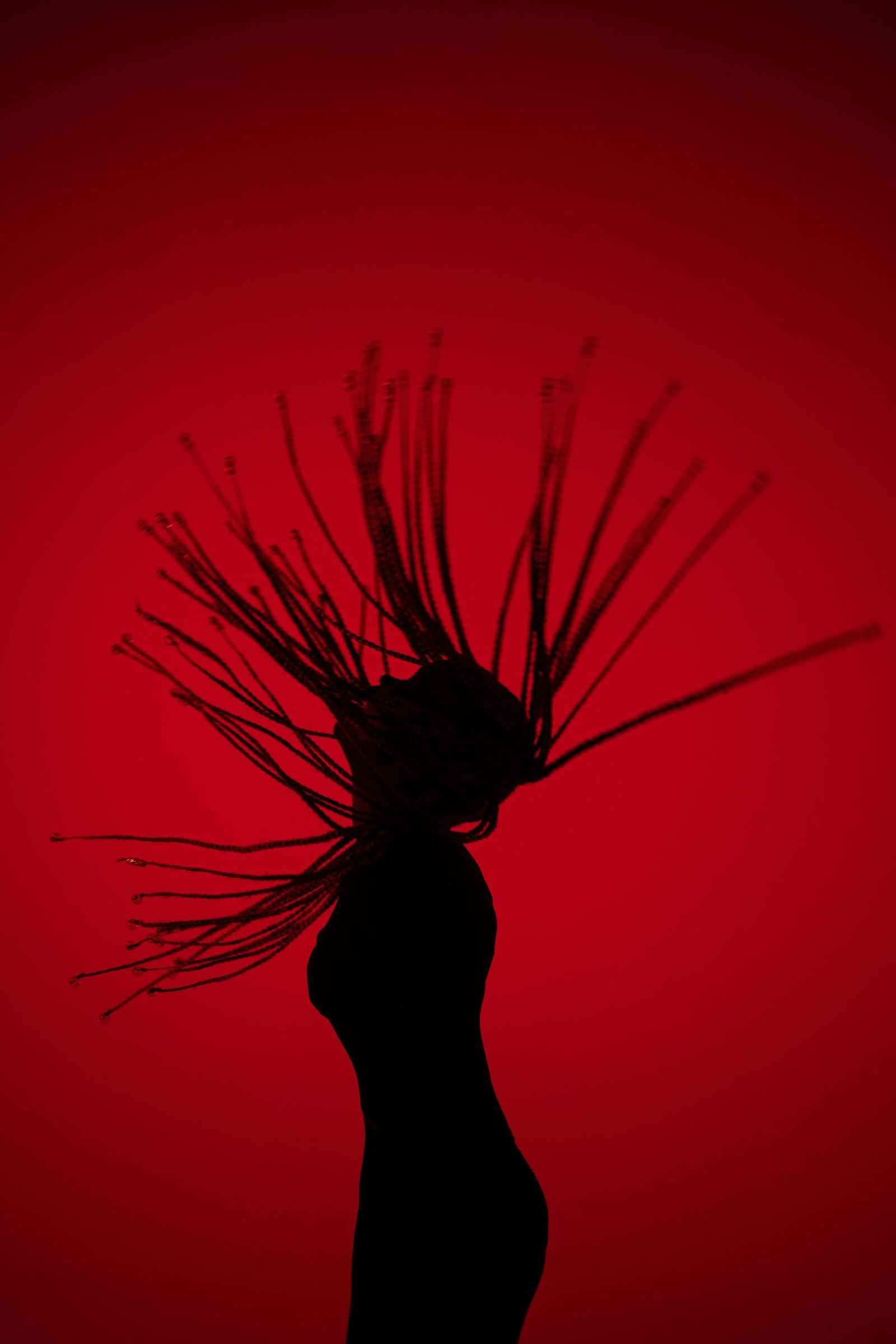 Silhouette of a person flipping their hair against a deep red background.