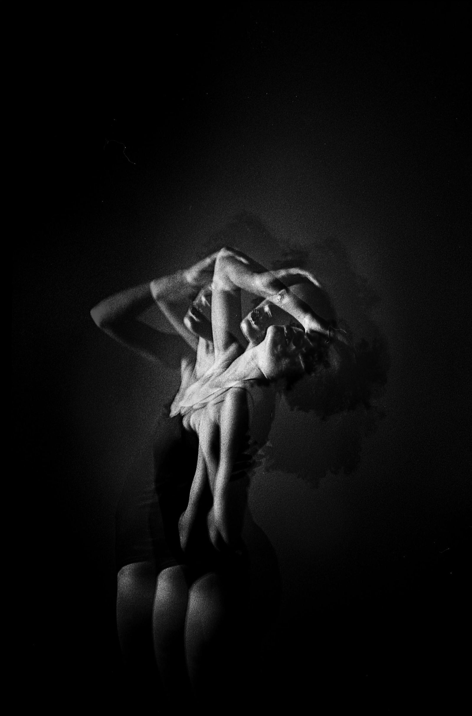 A person in dark clothing holds a pose under hard studio light.