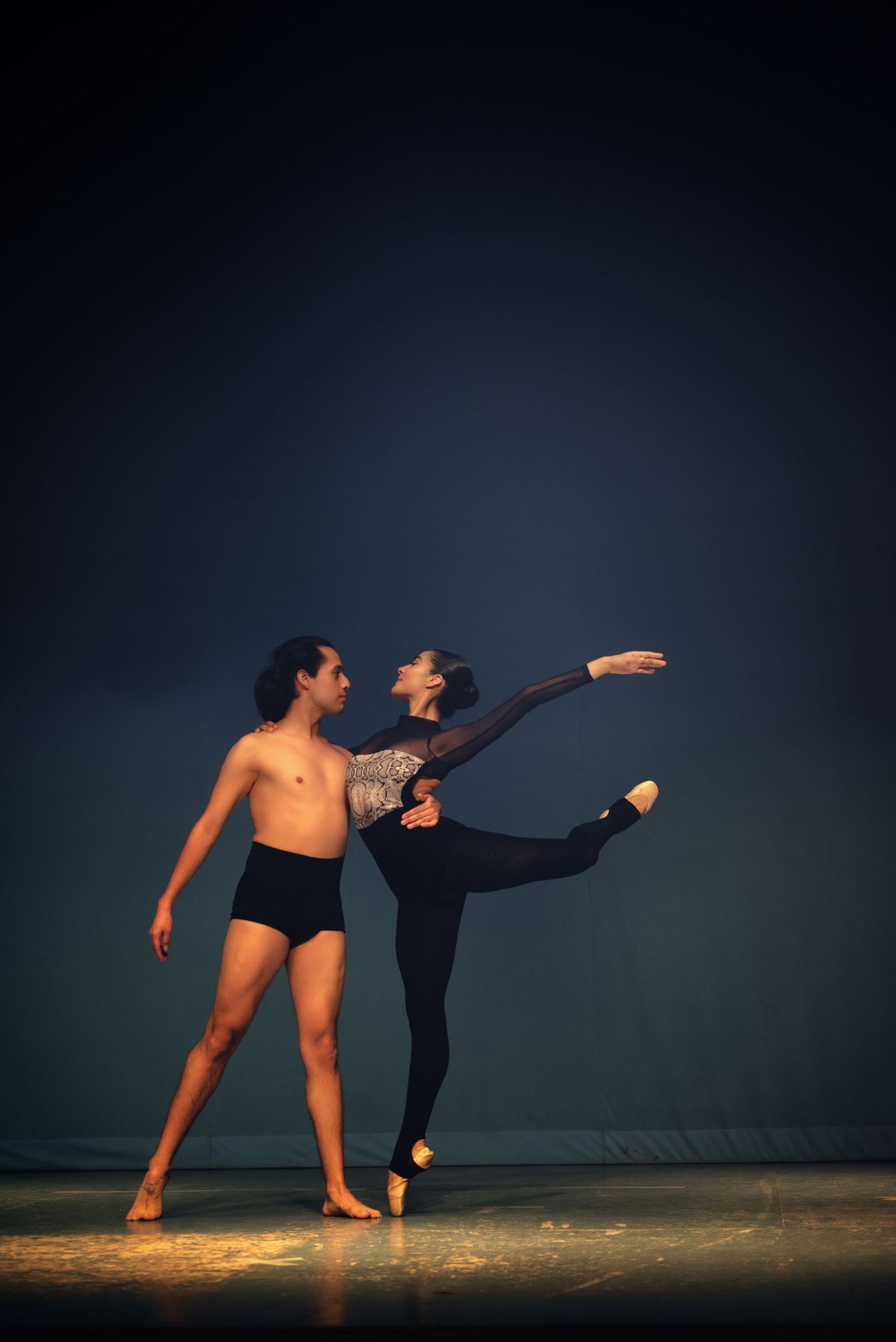 Dancers under a single spotlight on a dark stage.