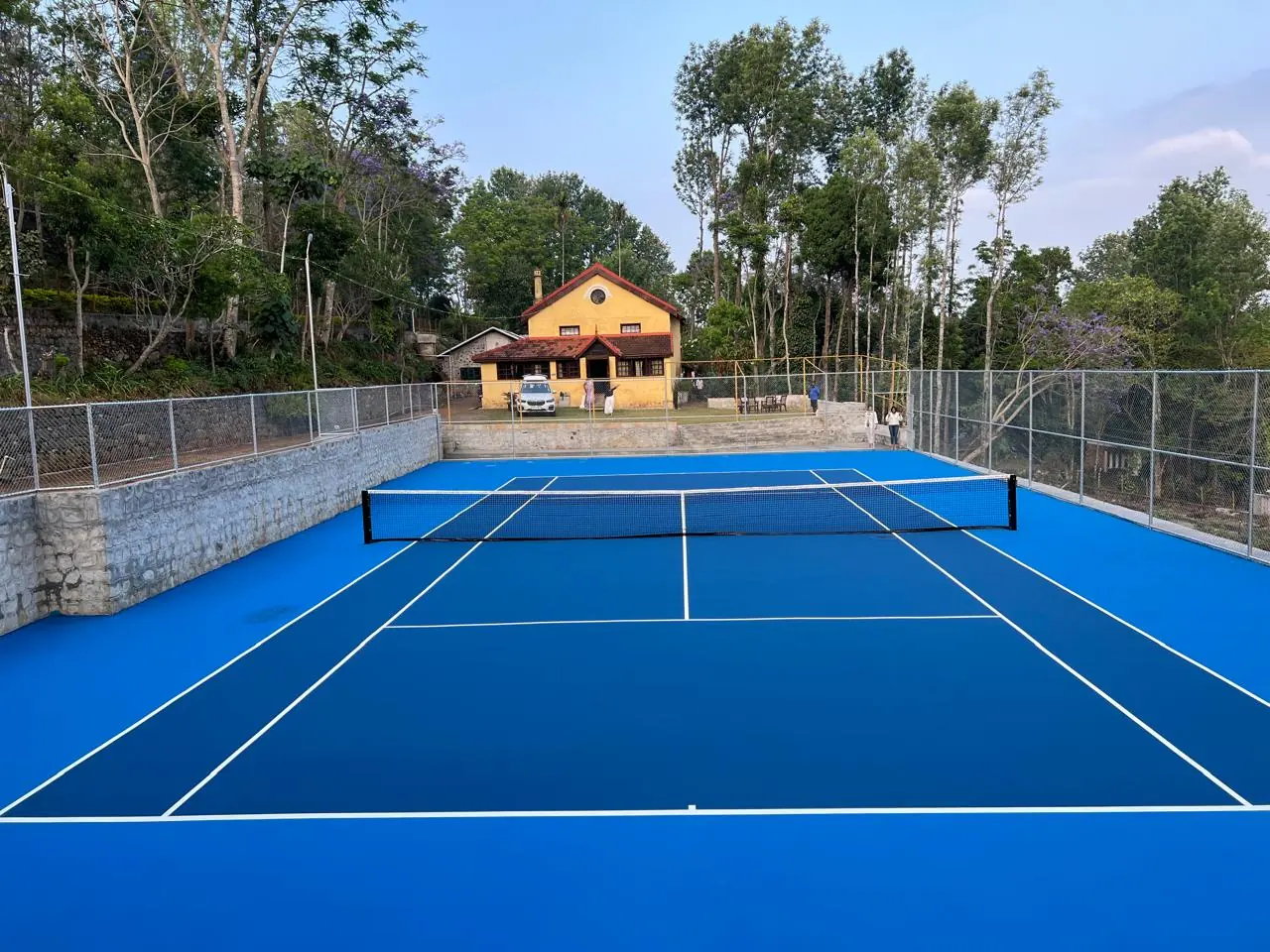 Blue tennis court beneath the trees, with the Yercaud Club building beyond